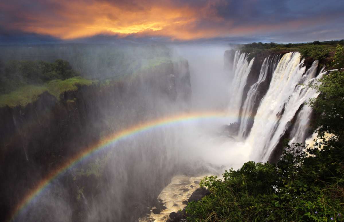 Victoria Falls in full flow during the high-water season (March–May), with thick mist rising and a rainbow forming over the gorge