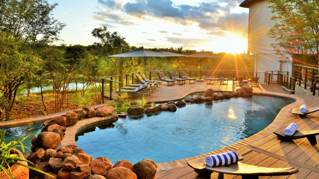 Luxury pool deck at Victoria Falls Safari Lodge with sun loungers, parasols, and a sunset over the Zambezi wilderness