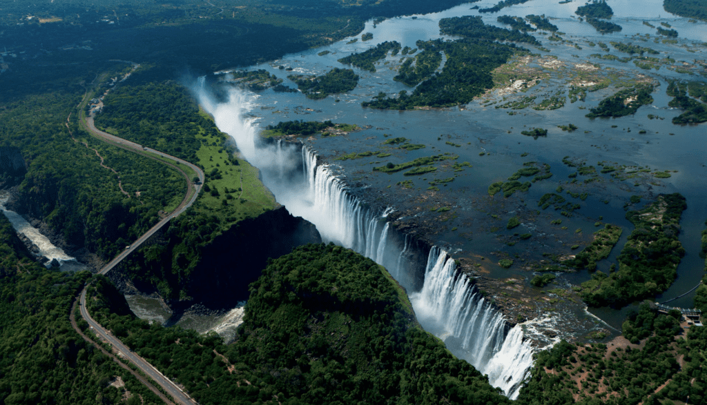 Aerial shot of Victoria Falls showing the Zambezi River, mist from the waterfalls, and the Victoria Falls Bridge linking Zambia and Zimbabwe