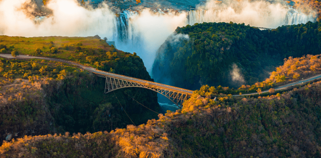 Aerial view of the Victoria Falls Bridge spanning the Zambezi Gorge with the mist of Victoria Falls rising in the background


