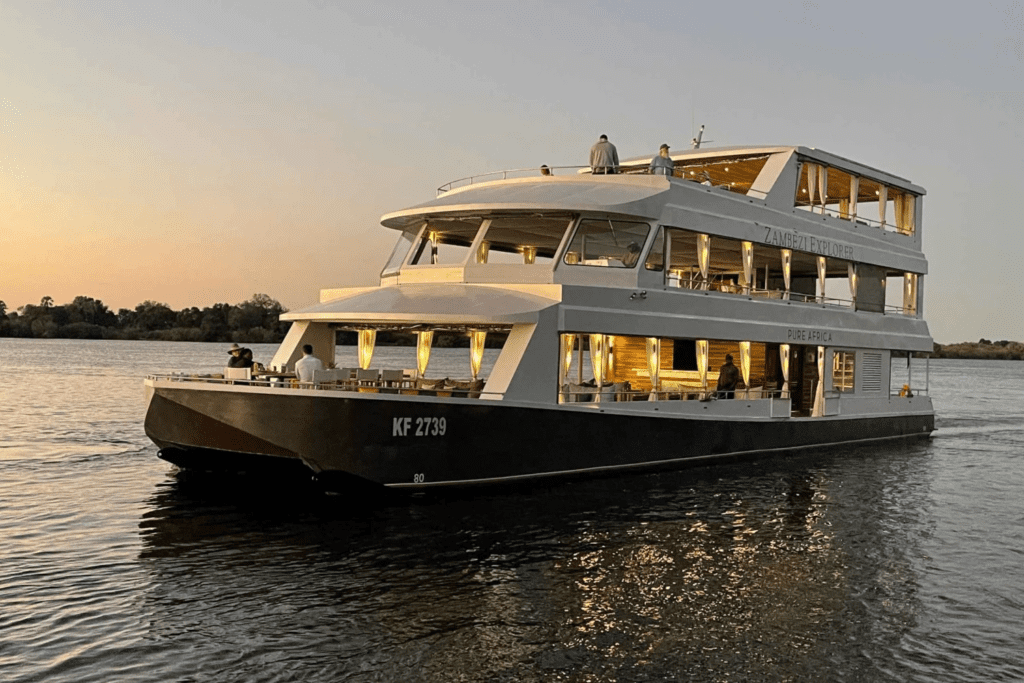 Guests enjoying a sunset dinner on a Zambezi River cruise near Victoria Falls, with candlelit tables, calm waters, and wildlife along the riverbank